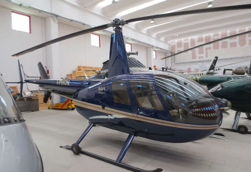 A dark blue Robinson R44 Raven I helicopter with the registration I-PHON is parked indoors.