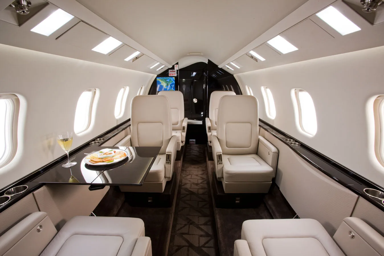 Aircraft interior with leather seats, a table with a glass of wine and a plate of food.