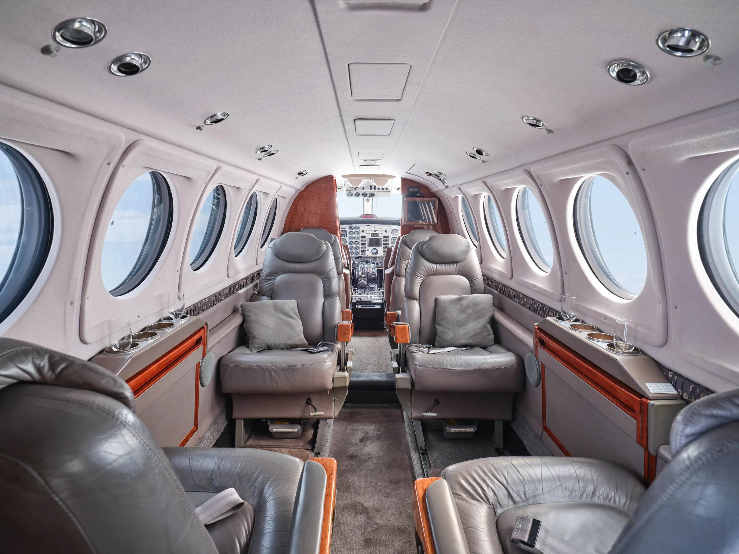 The aircraft cabin interior shows grey leather seating arrangements and a view towards the cockpit.