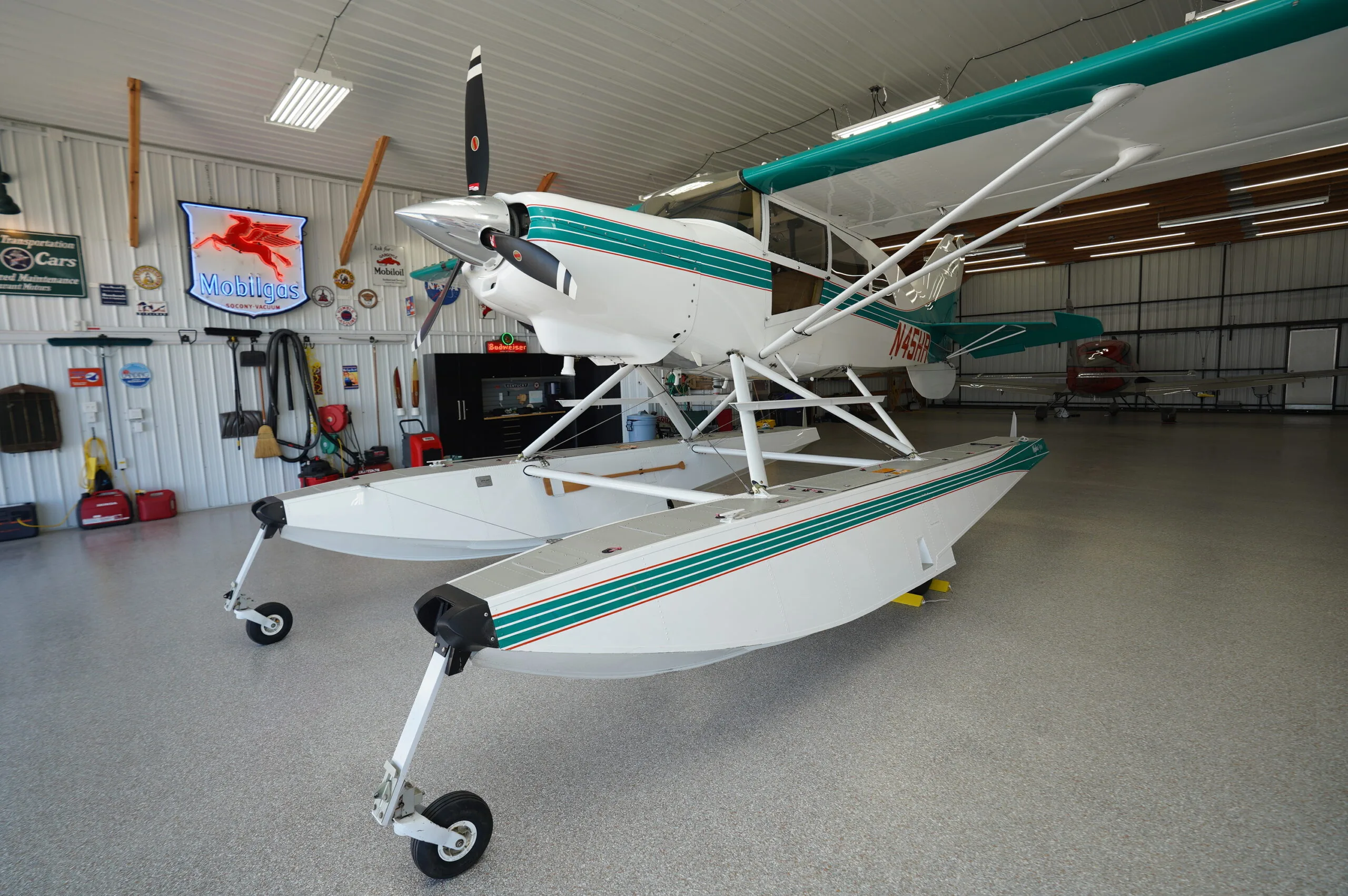 Front-left view of a white and teal floatplane with wheels, parked in a hangar.