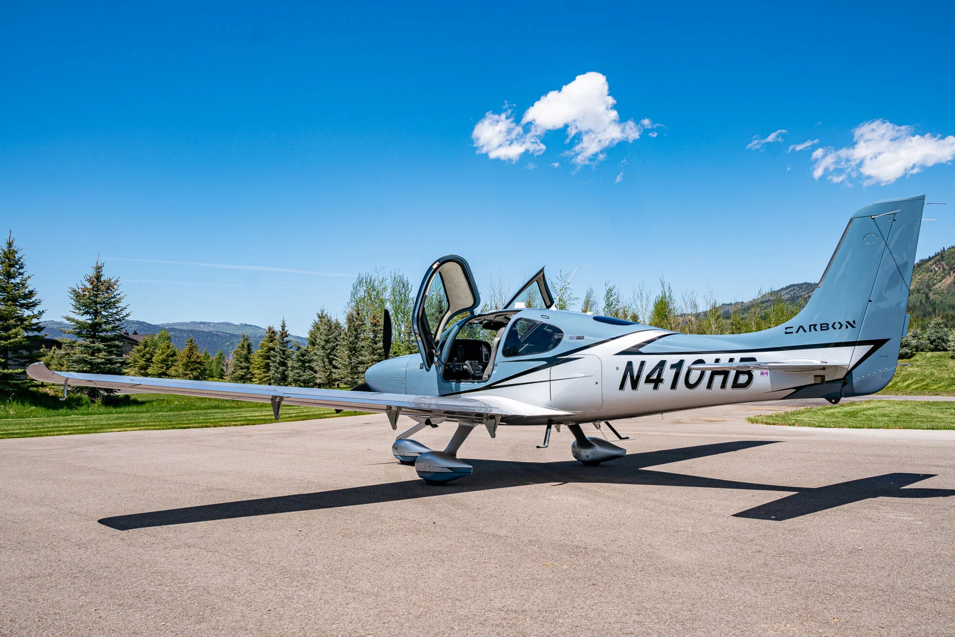 A light blue and silver Cirrus SR22T aircraft (N410HB) with its doors open, parked on an airfield.