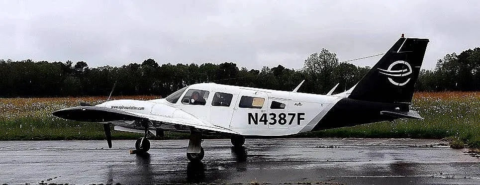 A white and black Piper PA-34 Seneca II, registration N4387F, parked on a wet tarmac with trees in the background.