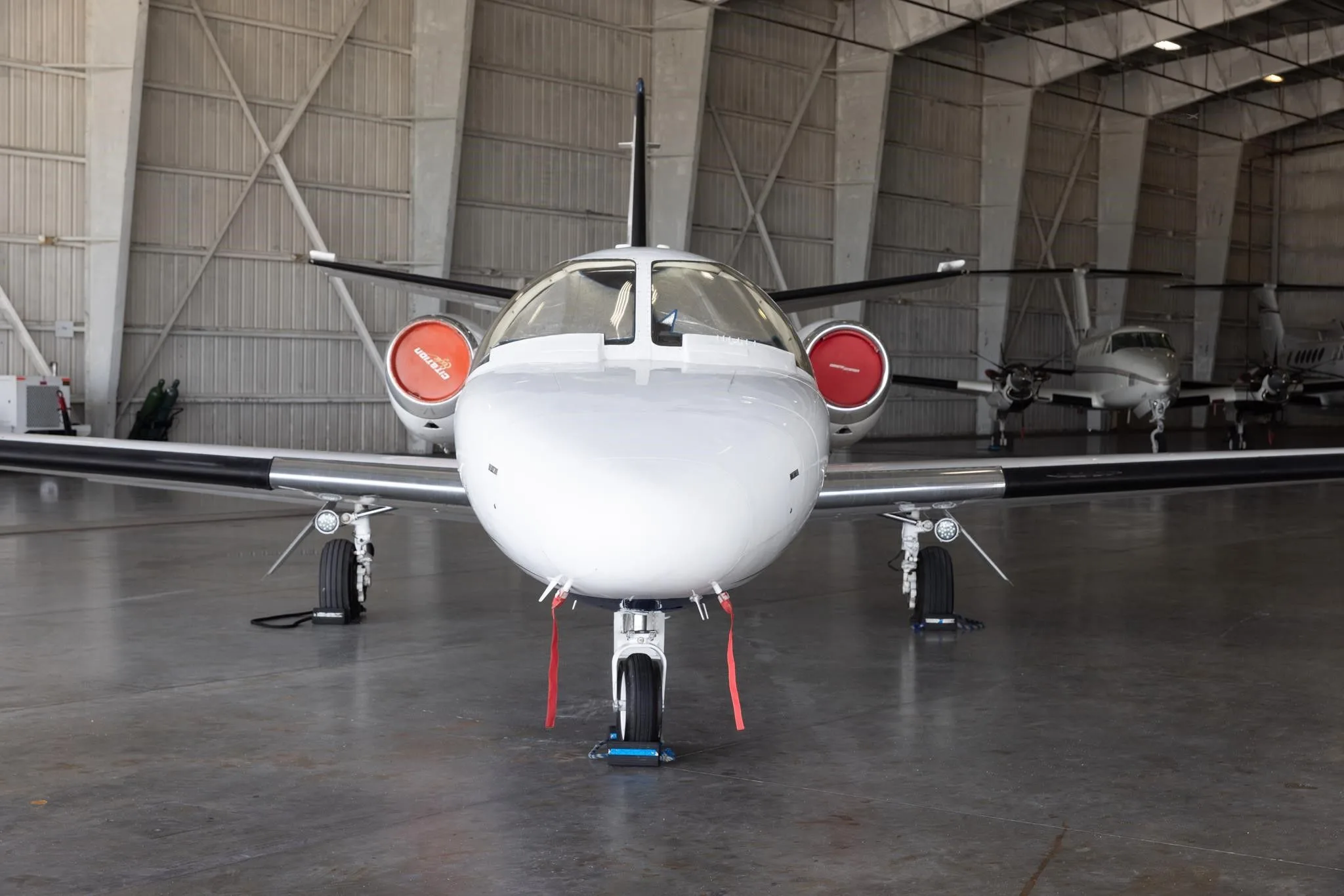 A head-on view of the white Cessna Citation jet (N3095M) with red engine inlet covers, inside a hangar.
