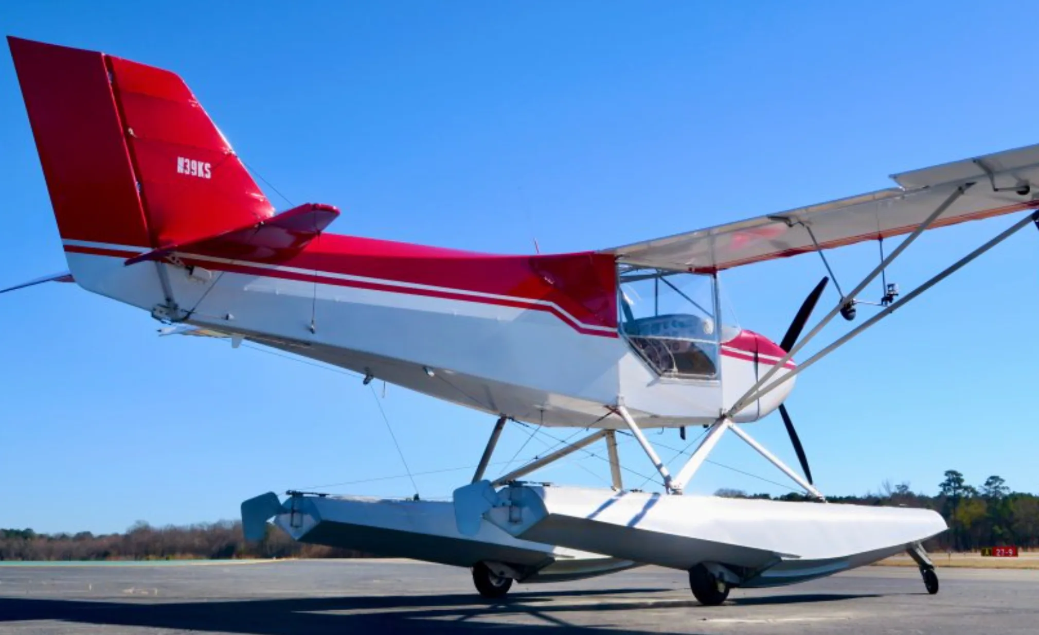 A three-quarter rear view of the red and white N39KS floatplane parked on an airfield under a clear blue sky.