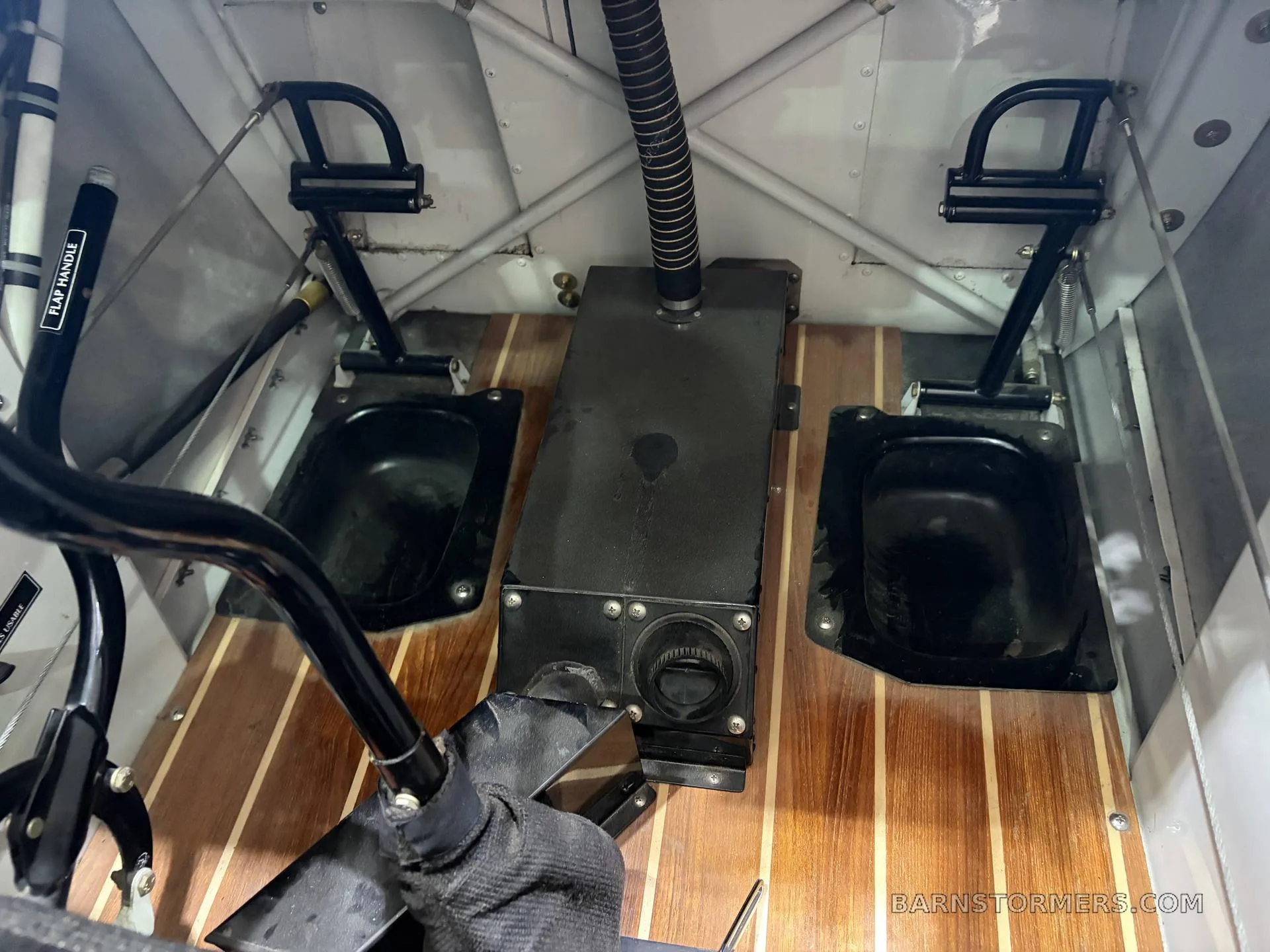 The wooden floorboards and rudder pedals of an aircraft cabin, with a flap handle visible on the left.