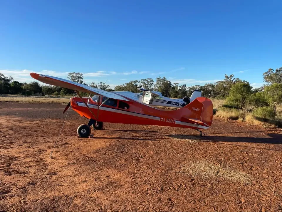 An orange and white high-wing aircraft with tail number 24-8804 parked on a red dirt field under a clear blue sky.