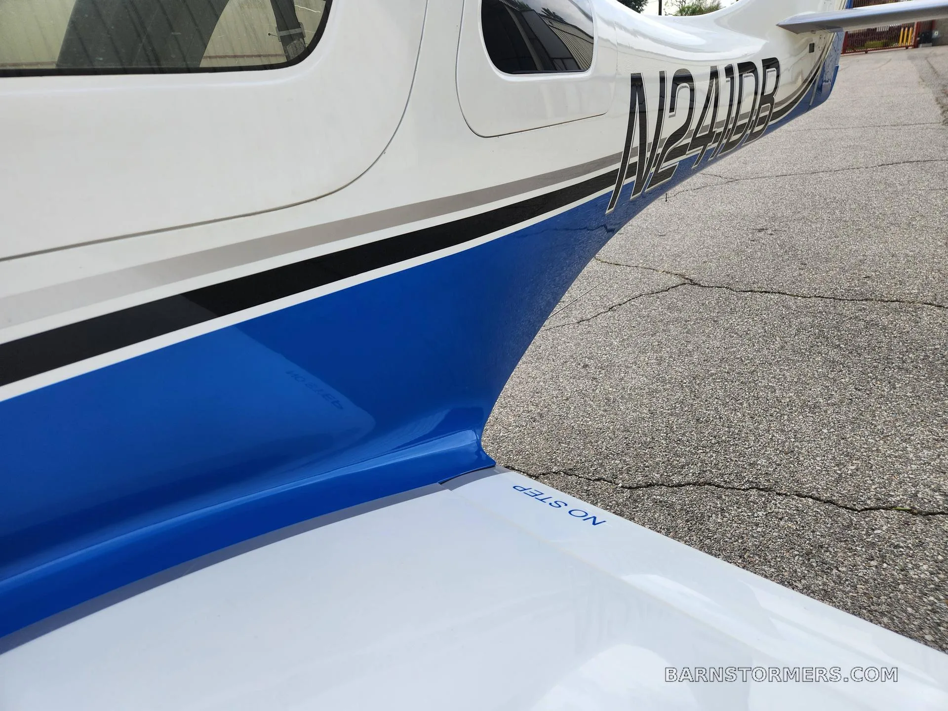 A close-up view of the white and blue fuselage and wing of an aircraft, showing the registration N241DB and "NO STEP" marking.