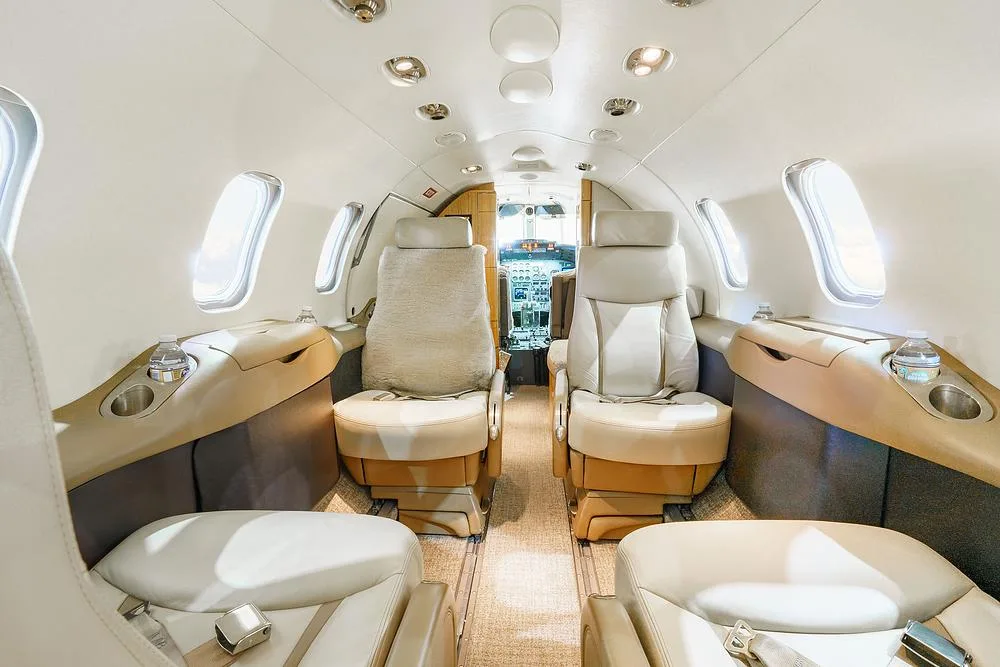 A view from the rear of the aircraft cabin looking forward, showing light-colored leather seats and the cockpit visible through the open door.