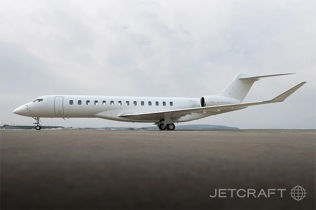A white Bombardier Global 7500 business jet is parked on a tarmac under a cloudy sky.