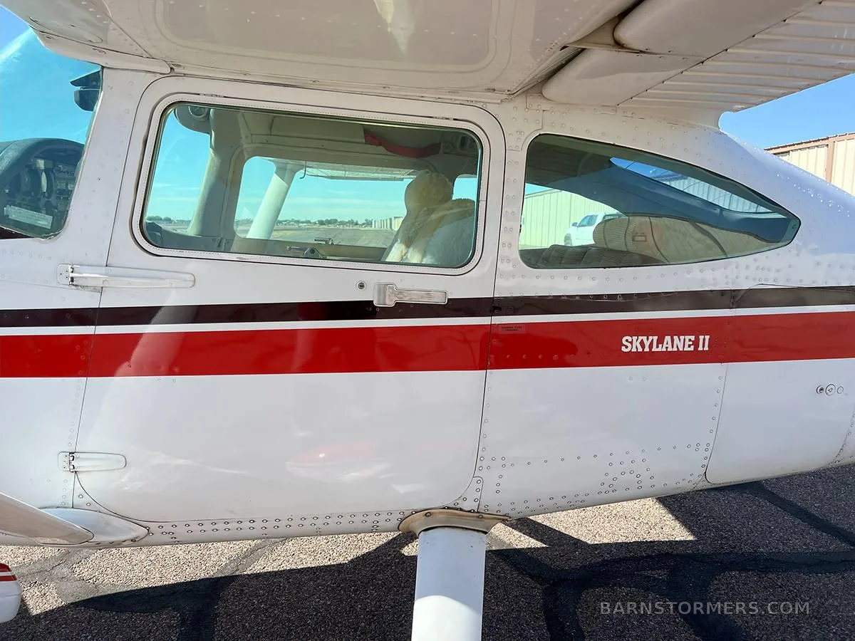 A close-up of the side fuselage of a white and red Cessna Skylane II, showing the cabin windows and "SKYLANE II" text.