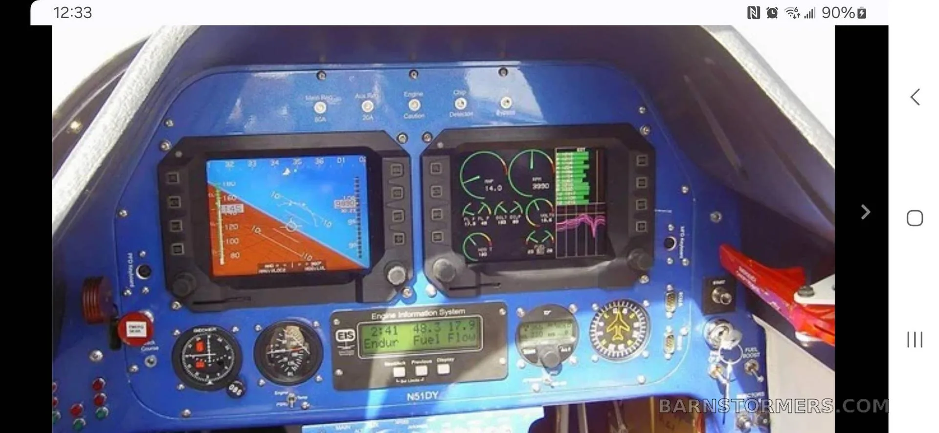 The blue cockpit panel of an aircraft, featuring two large digital displays and various analog gauges.