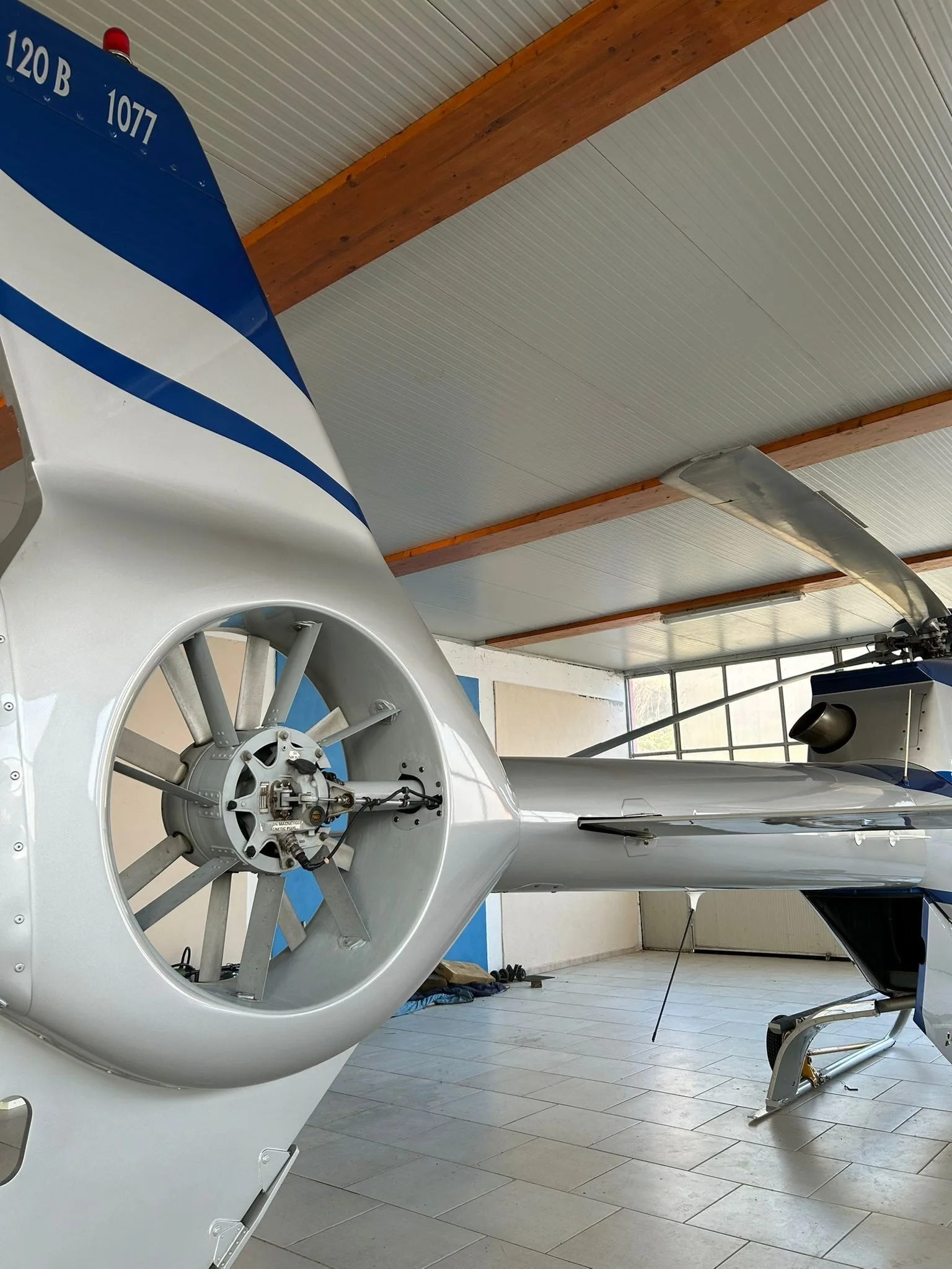 Close-up view of the Fenestron tail rotor and tail boom of an Airbus H120 Colibri helicopter inside a hangar.