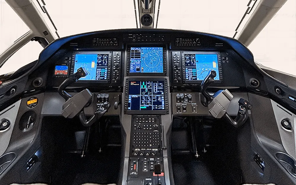 The modern glass cockpit of a Pilatus PC-12 NG, featuring multiple large display screens and control yokes.