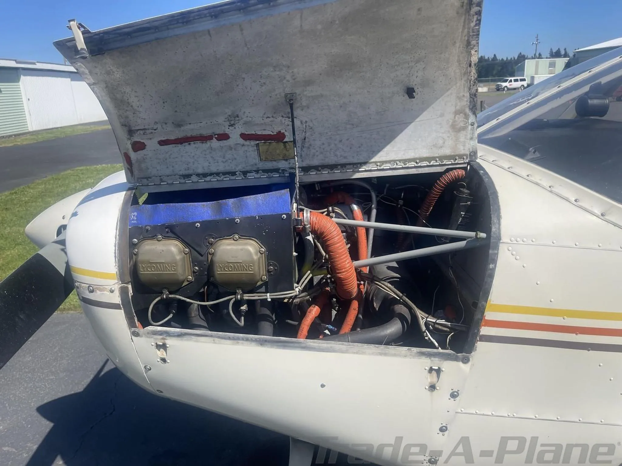 Close-up view of the aircraft's engine compartment with the cowling open, showing Lycoming engine components and orange hoses.