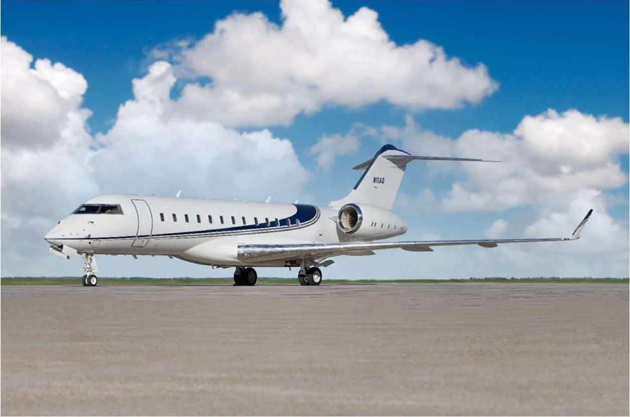 A white Bombardier Global business jet with blue stripes is parked on a tarmac under a partly cloudy sky.