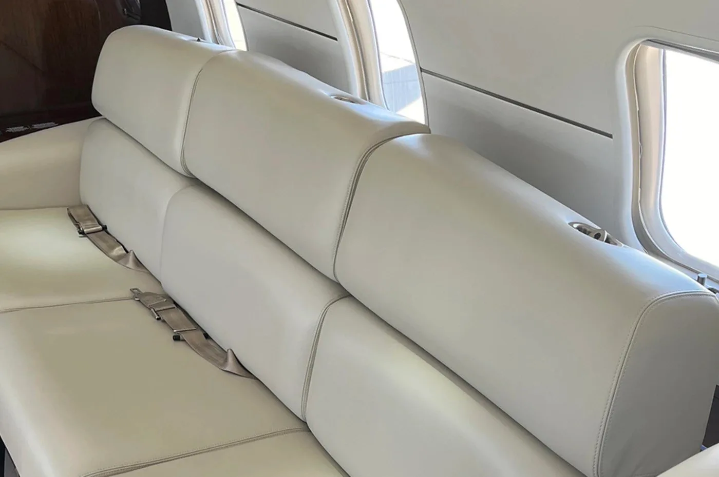 A close-up view of a light-colored leather bench seat with seatbelts in the aircraft cabin.