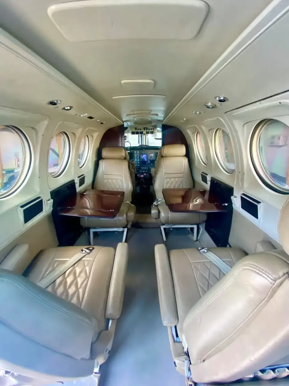 The aircraft cabin interior with tan leather seats and tables, looking towards the cockpit.