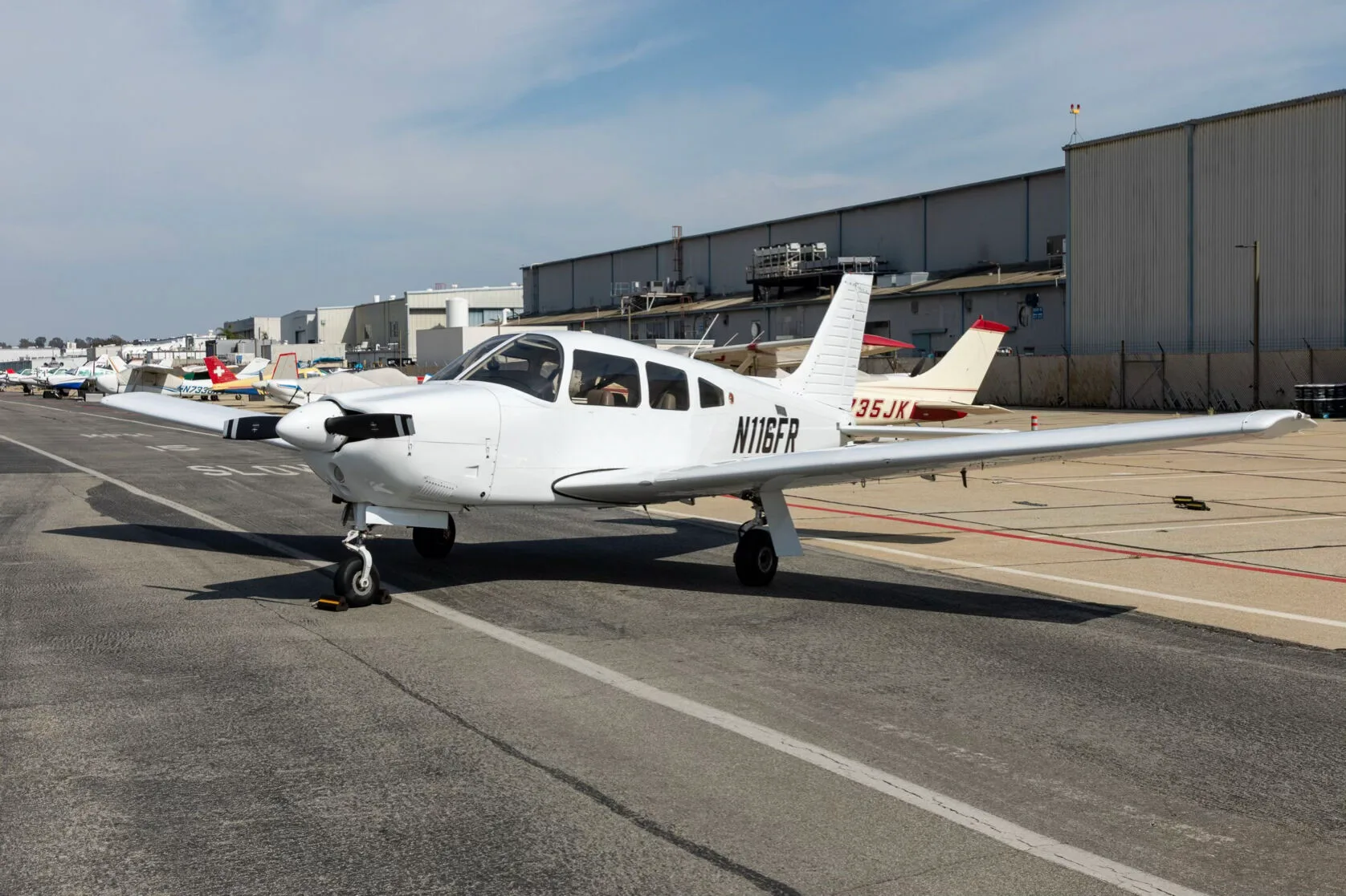 A white Piper PA-28-181 Archer III aircraft, registration N116FR, parked on an airfield next to other aircraft.