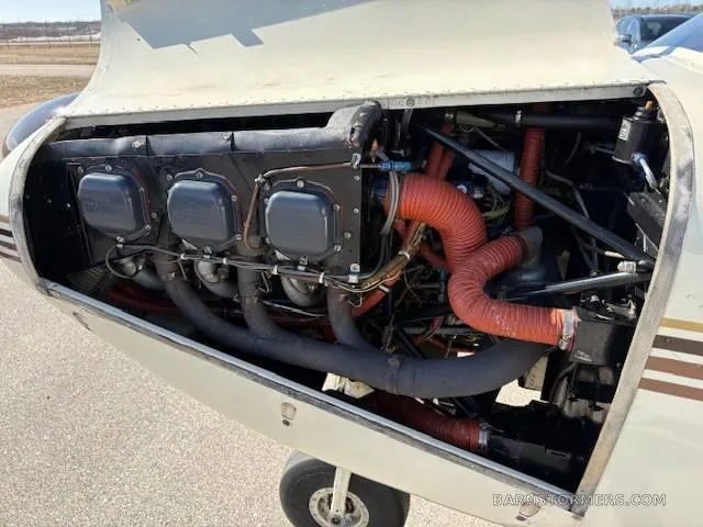 The open engine cowling of a Piper Comanche 250, revealing the engine with its black cylinders and red hoses.