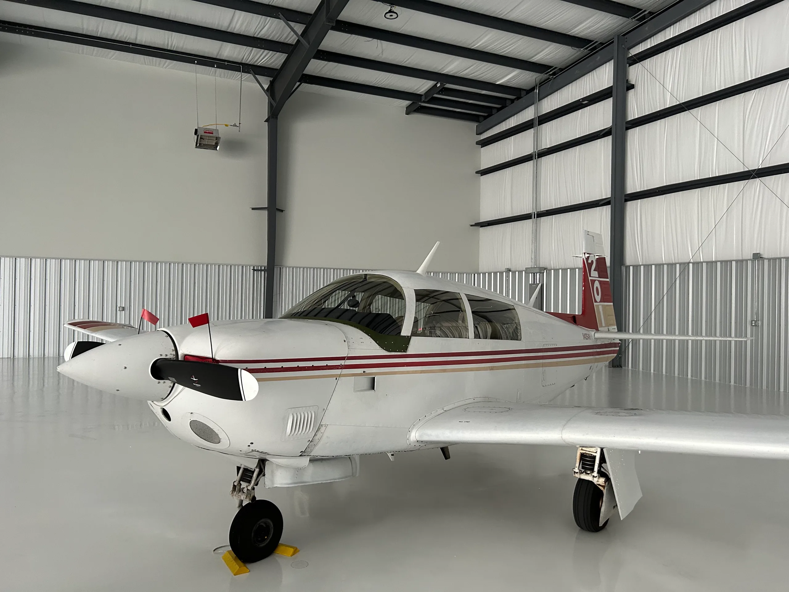 A white single-engine aircraft with red and gold stripes on the tail and fuselage, parked inside a hangar.