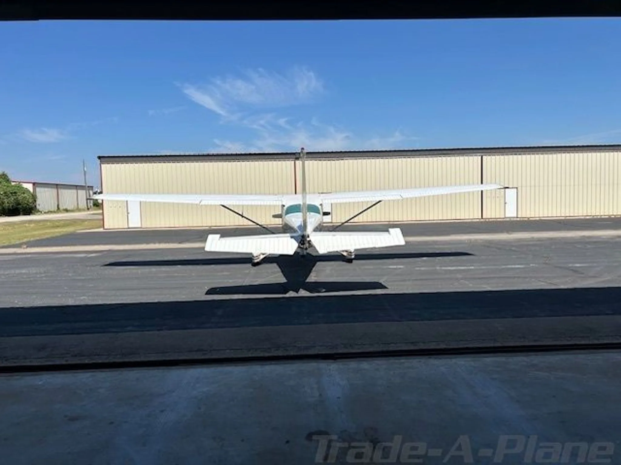 Rear view of a white and brown Cessna R172K parked on an asphalt ramp, seen from inside a hangar.