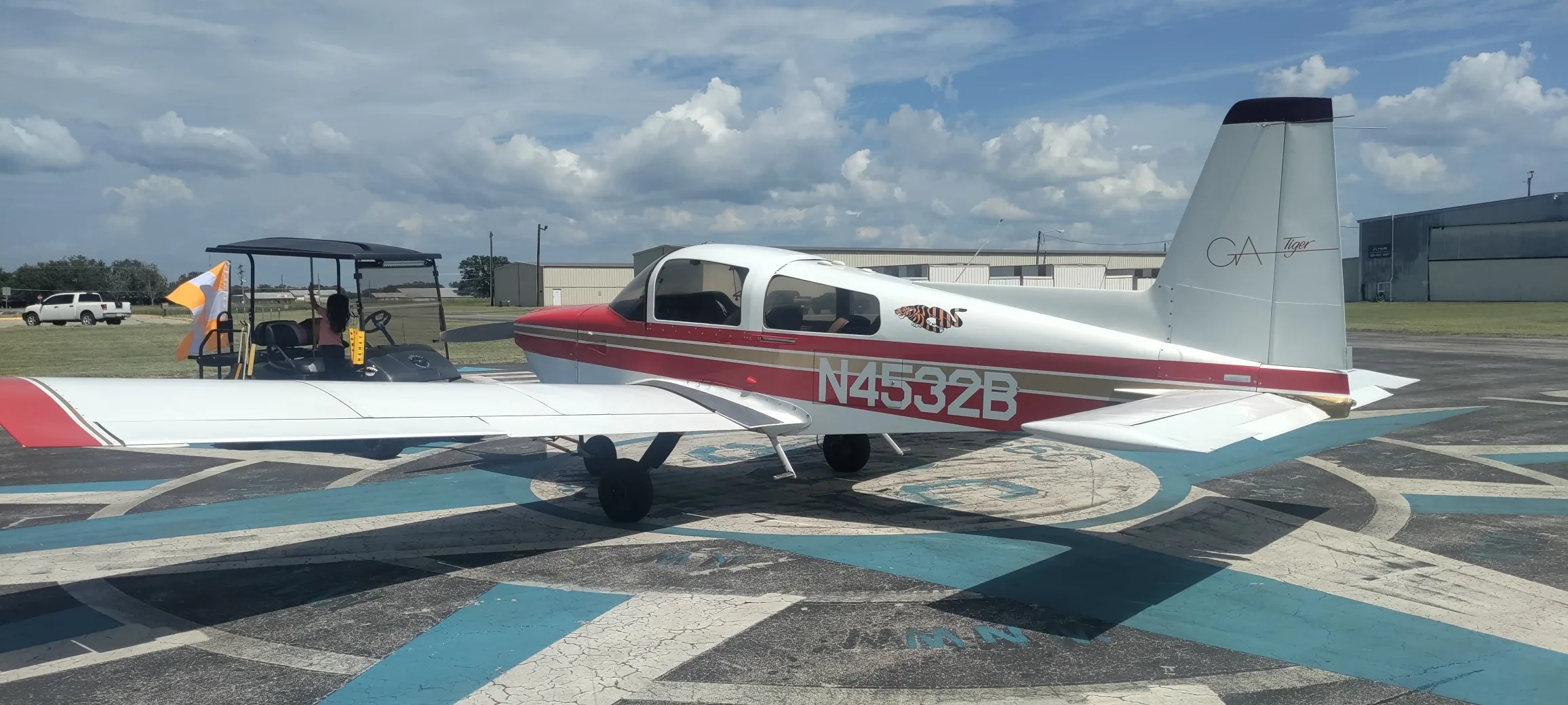 A red and white Gulfstream American GA-7 Cougar aircraft, N4532B, parked on an airfield with a golf cart nearby.