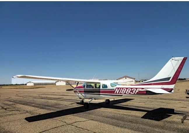 A side view of a white and maroon Cessna 210 Centurion aircraft with registration N1883F parked on an airfield.