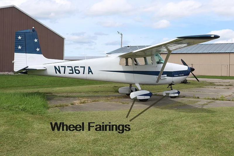 A white and blue Cessna 170 aircraft with registration N7367A parked on grass next to a hangar.