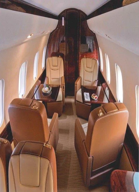 The rear section of a private jet cabin featuring brown and beige leather seats and small tables with refreshments.