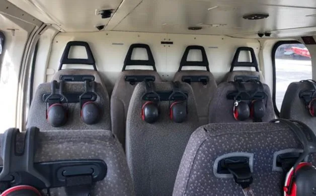 The interior cabin of a helicopter features multiple rows of grey passenger seats with headsets.