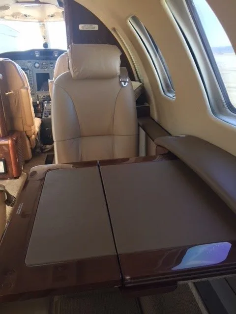 Aircraft interior with a tan leather seat, fold-out table, and view of the cockpit.