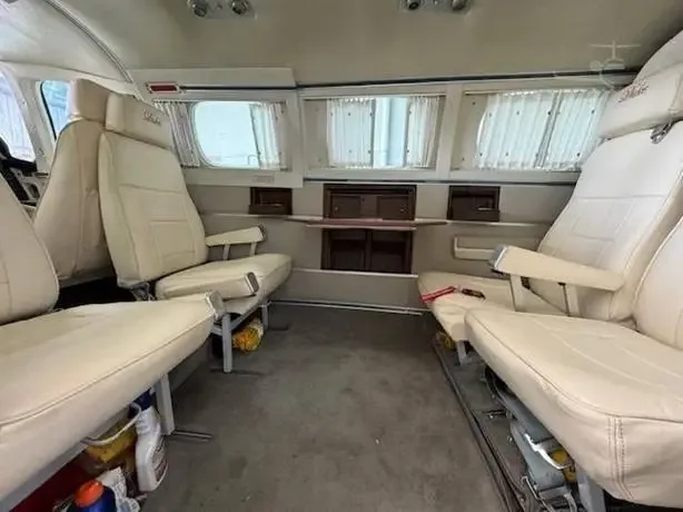 The aircraft cabin features cream leather seats, window curtains, and a small table between facing seats.