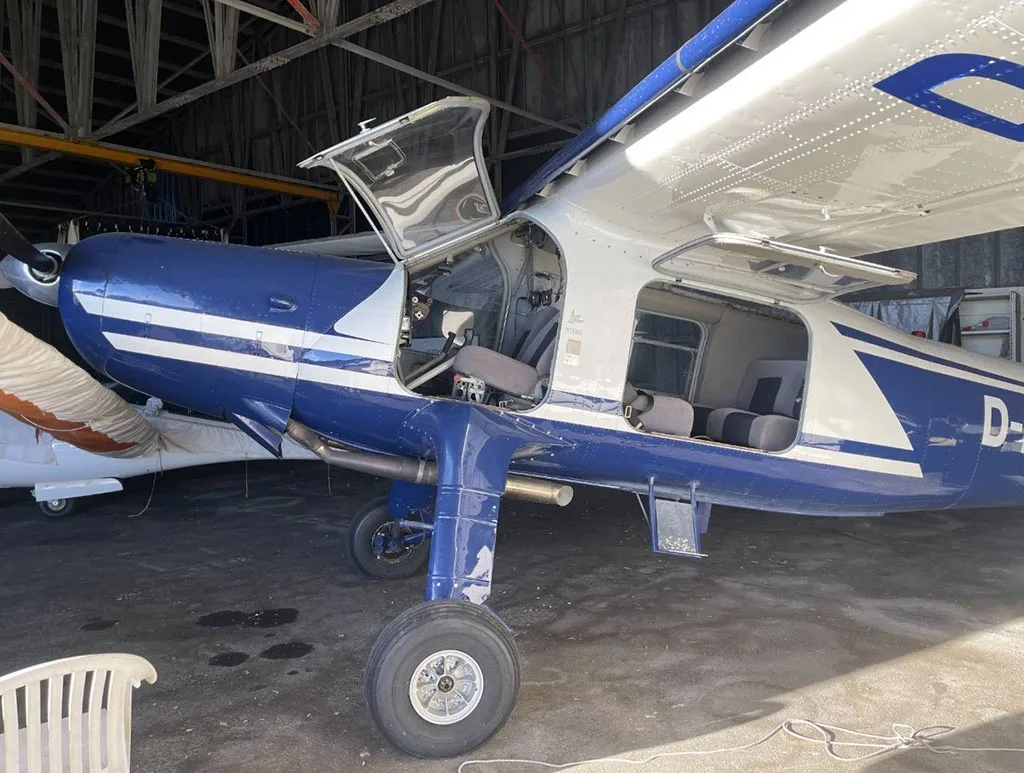 The front-left side of a blue and white aircraft, D-EOAC, with its doors open, parked inside a hangar.