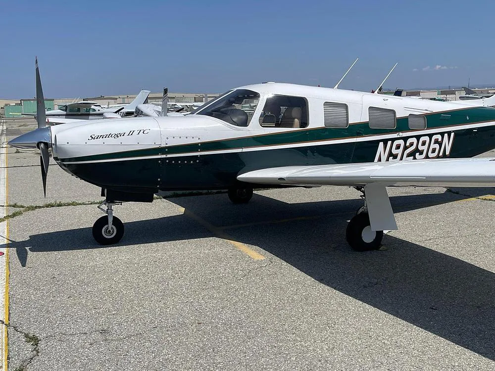 A side view of the Piper Saratoga II TC, registration N9296N, in dark green and white, parked on an airfield.