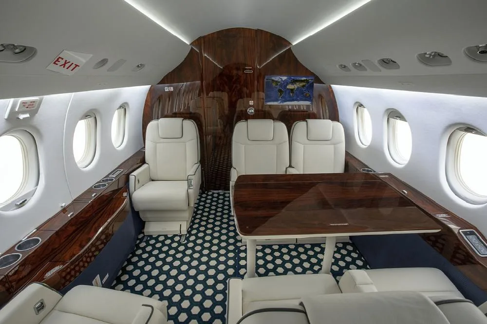 A view of the business jet's cabin with white seats, a dark wood table, and a world map displayed on a screen.