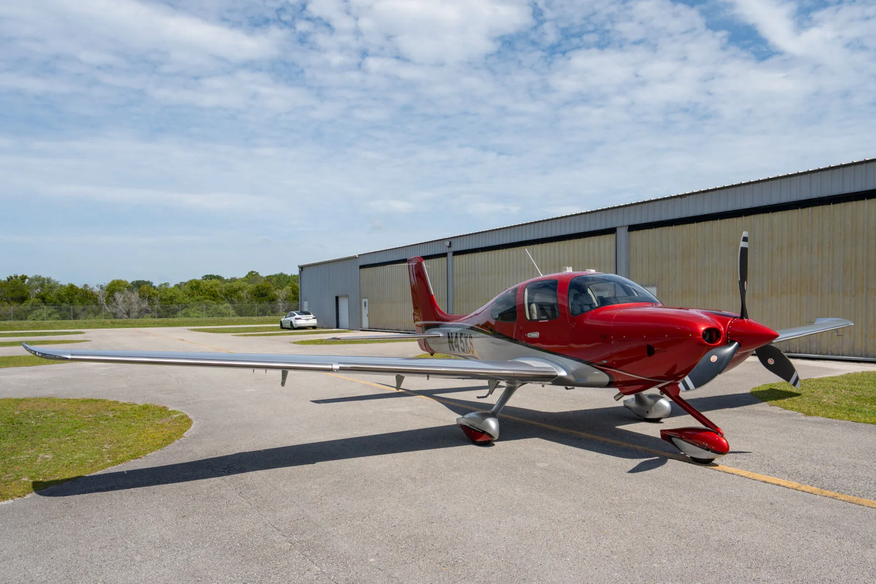 A red and silver Cirrus SR22 GTS (N45KS) parked on an airfield next to a hangar.