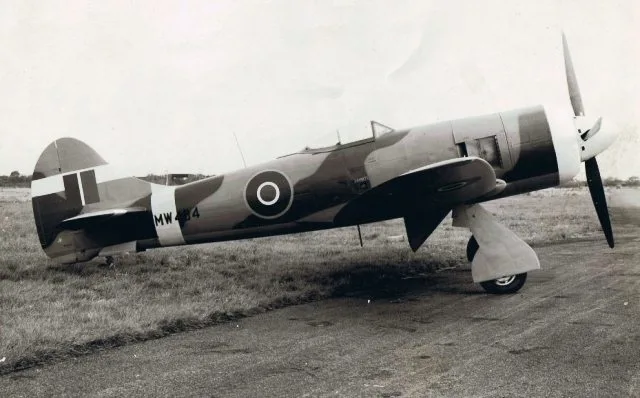 A Hawker Tempest fighter aircraft in camouflage paint scheme parked on a tarmac with grass.