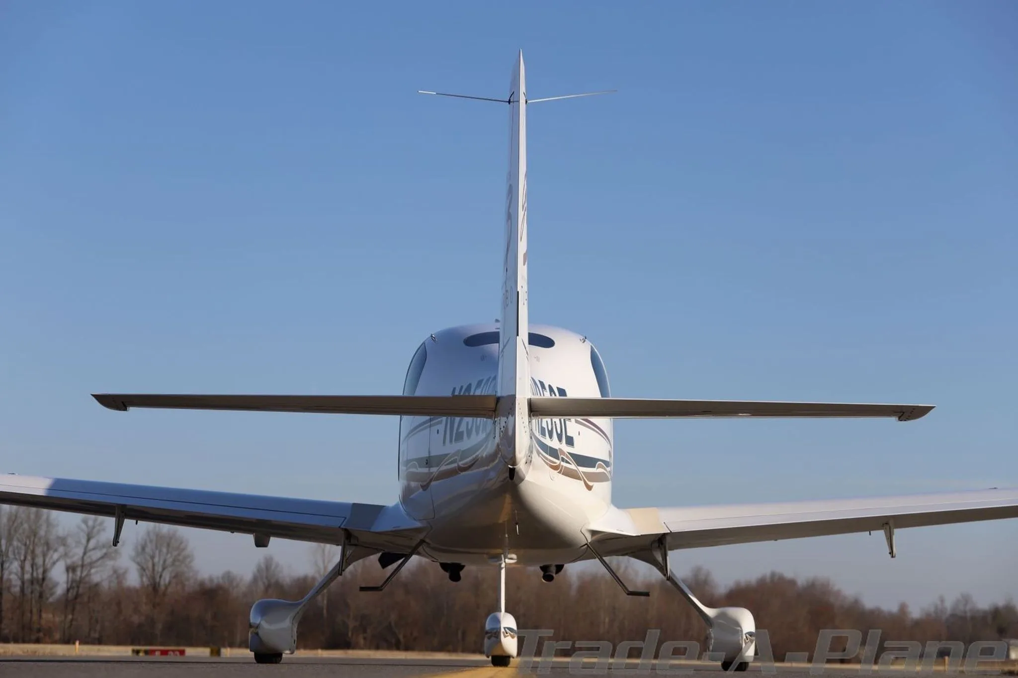 Rear view of a white Cirrus SR22T aircraft (N253E) with gold and brown accents, parked on an airfield.