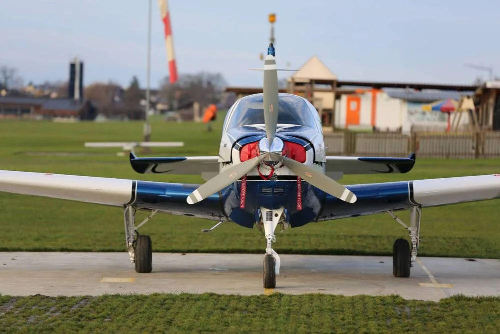 A front view of a blue and white single-engine propeller aircraft on a concrete pad at an airfield.