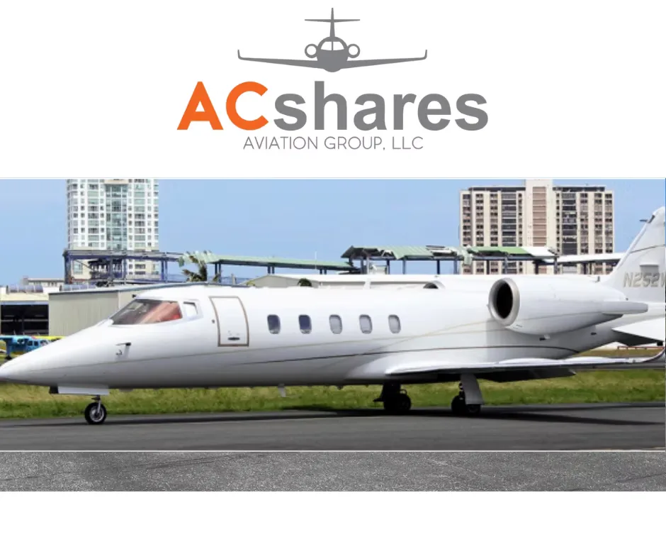 A white business jet, tail number N252W, sits on an airfield with urban buildings behind it.