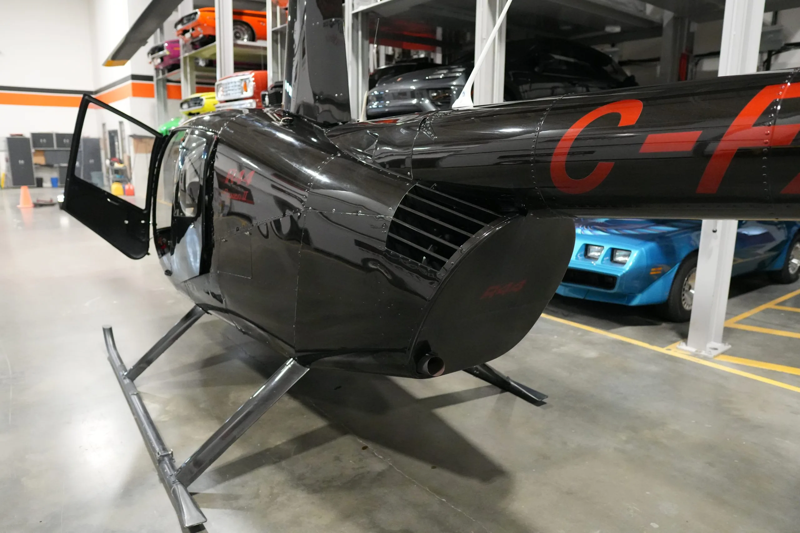 A close-up view of the black Robinson R44 helicopter's tail boom and exhaust, with an open door.