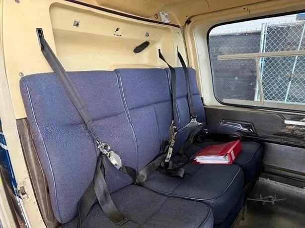 The rear bench seat of a helicopter cabin, upholstered in blue fabric with seatbelts.