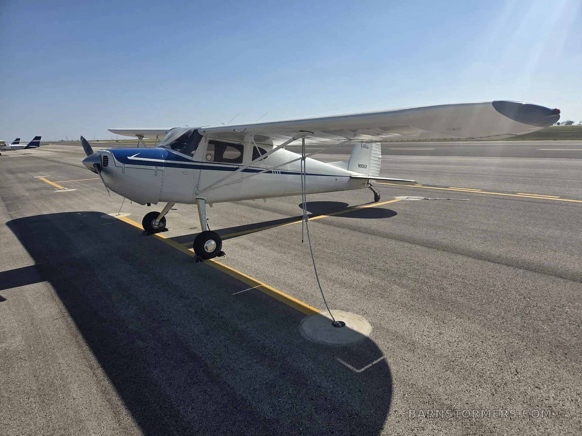 A white and blue Cessna 120 aircraft with tail number N90113 parked on an airport tarmac on a sunny day.