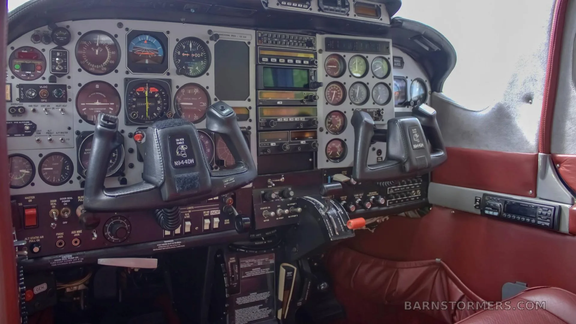 The cockpit of an aircraft, showing the instrument panel with analog gauges, avionics, and two control yokes.