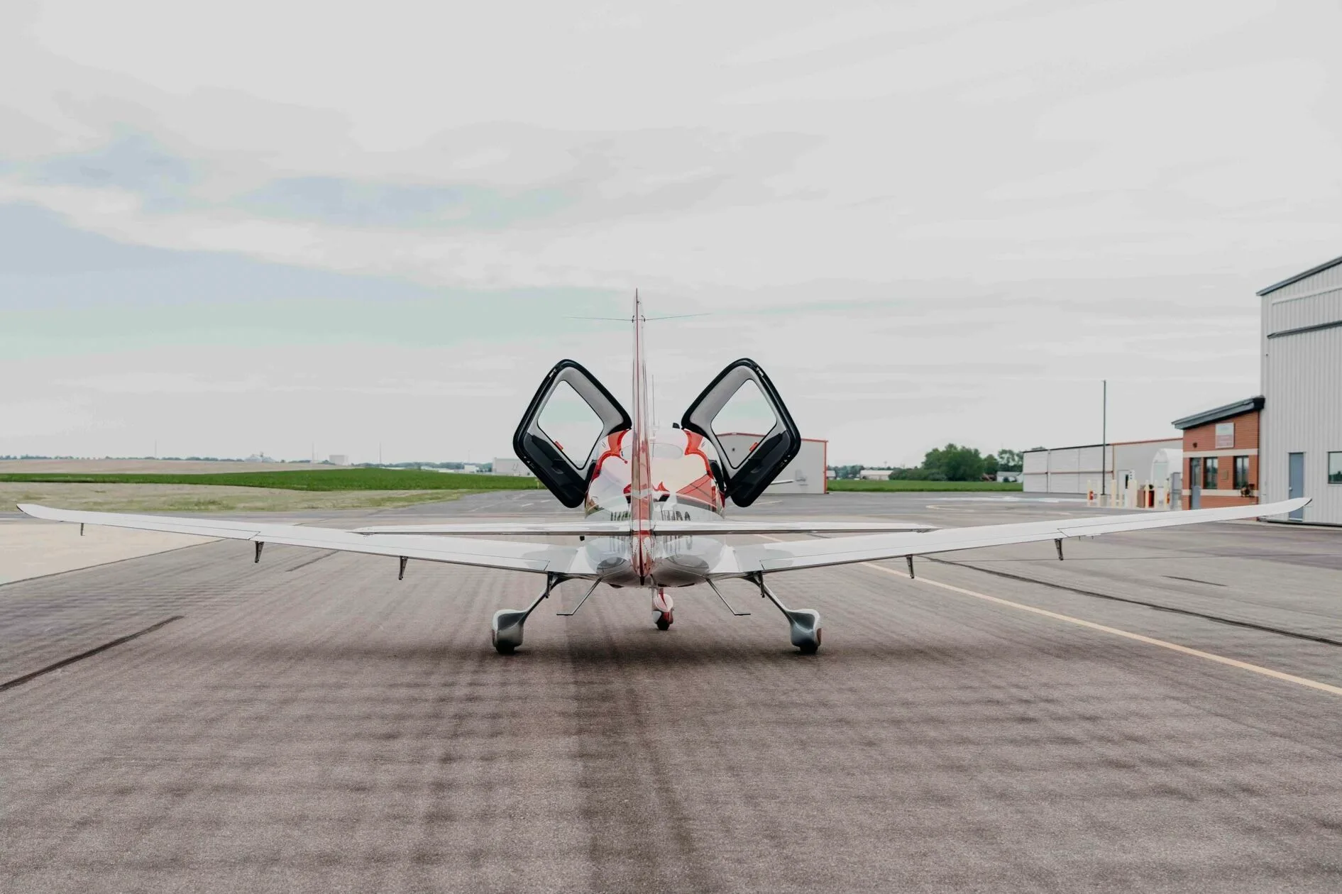 A rear view of the red and silver Cirrus SR20 Premium aircraft (N11PS) with both doors open, parked on the tarmac.