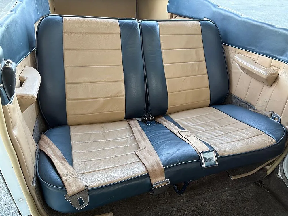The rear two-tone blue and tan leather seats of an aircraft cabin with seatbelts fastened.