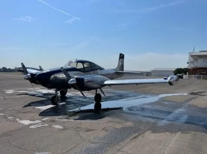 A silver and blue twin-engine aircraft, N708T, parked on a wet tarmac at an airport.