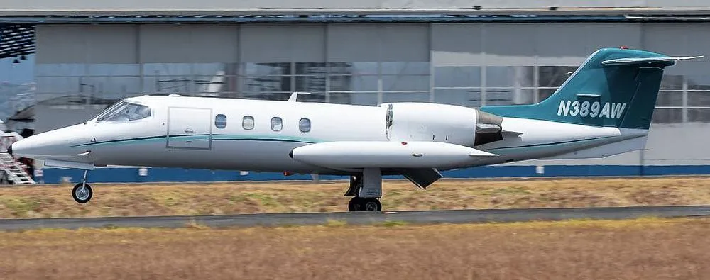 A white Learjet 35A with a teal tail, registration N389AW, is shown on a runway with its landing gear extended.