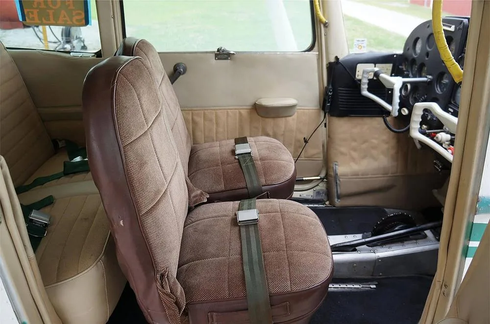 The tan and brown fabric interior of a small aircraft cabin, showing two front seats and a partial view of the rear seat.