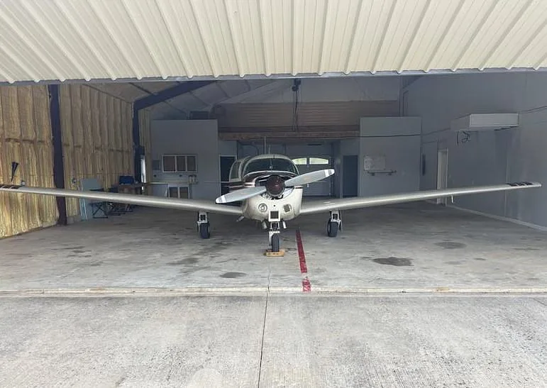 A Mooney M20 aircraft, registration N6933N, viewed head-on inside a hangar with the door open.